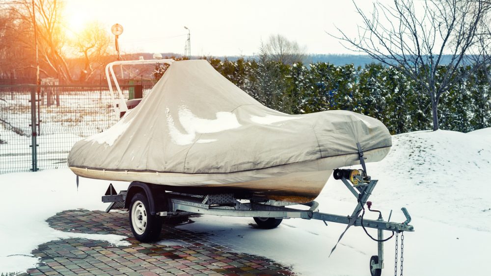 A small, covered boat on a trailer in the snow.