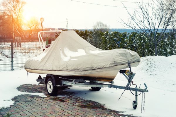 A small, covered boat on a trailer in the snow.